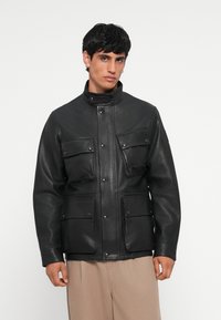 Black leather jacket with a high collar, snap closures, and four front pockets. Smooth texture and tailored fit.