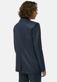 Marineblauer, maßgeschneiderter Blazer mit glatter Textur, einem einzelnen Schlitz und abgesteppten Revers. Der Rücken ist tailliert und strukturiert.