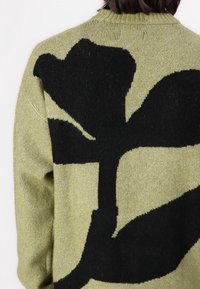 Zielony sweter dziany z dużym czarnym wzorem kwiatowym na plecach, z prążkowanym dekoltem i fakturowaną tkaniną.