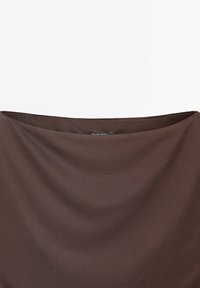 Tissu marron avec une texture lisse et drapée. Le bord supérieur est doucement arrondi. Une étiquette noire est visible près du coin supérieur gauche.