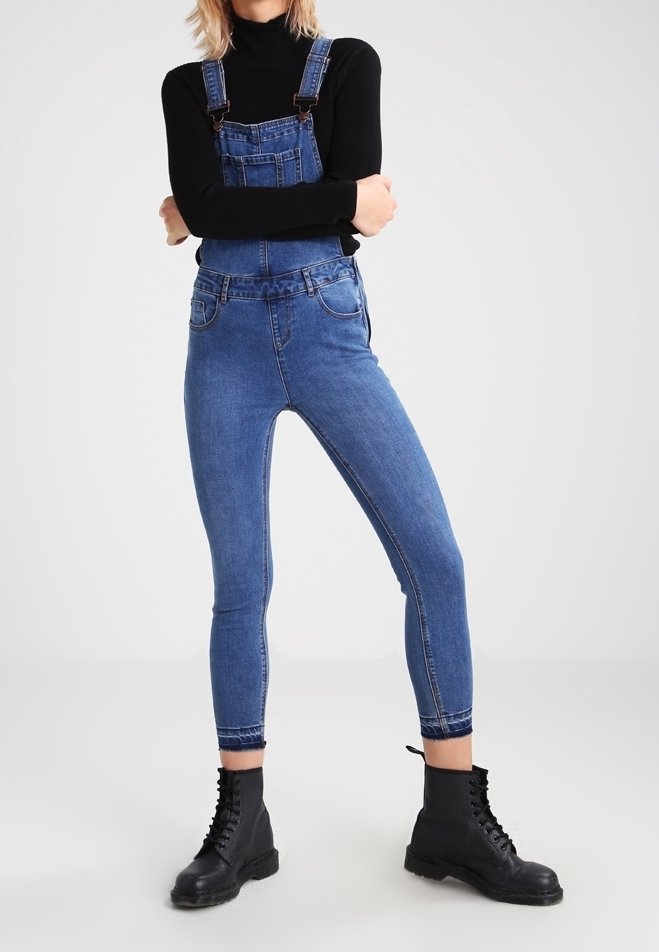 Jeansoveraller i medelblått med en figurnära silhuett, justerbara remmar och framfickor, kombinerat med svarta snörda kängor.