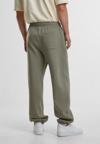 Olivengrønne sweatpants med elastisk talje, manchetter og en baglomme, parret med hvide sneakers. Blødt materiale, afslappet pasform.