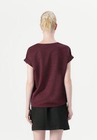 Burgundy kortärmad topp med en subtil glans, med rullade ärmar och en avslappnad passform, ihop med en svart kjol.