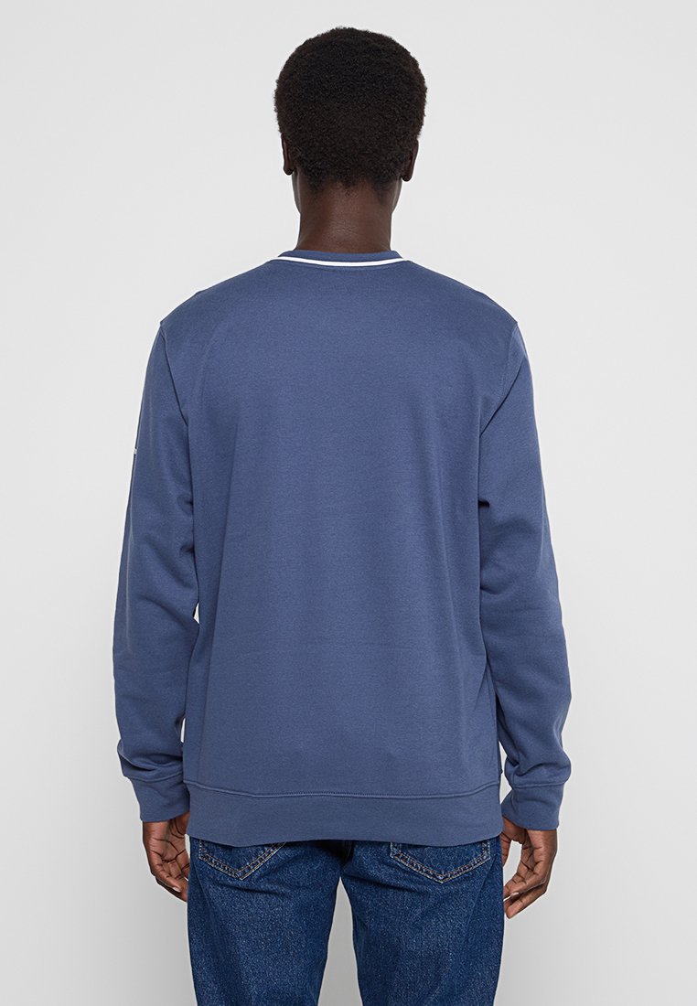 Felpa blu navy con maniche lunghe, collo rotondo e dettagli di cucitura bianca al colletto. Tessuto liscio con una vestibilità comoda.