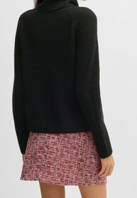 Svart stickad polotröja med ribbad textur, kombinerad med en mönstrad minikjol i texturerat rosa och vitt.