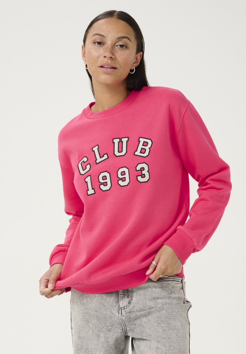 Rosa Sweatshirt mit der Aufschrift "CLUB 1993" in weißen und schwarzen Buchstaben. Hergestellt aus weichem Stoff mit gerippten Bündchen und Saum.