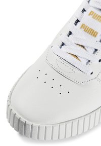 Zapatillas de piel blanca con detalles perforados, suela de goma texturada y cordones blancos con acentos dorados en la lengüeta.