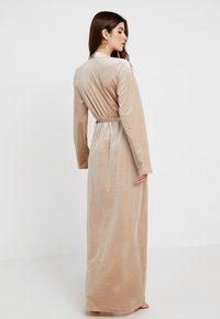Accappatoio lungo in velluto beige con maniche lunghe, vita con cintura e una texture liscia. Presenta un design semplice con una silhouette fluente.