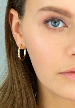 Gold hoop earring with a twisted design, featuring a polished surface and smooth texture. Close-up showing earring worn on the ear.
