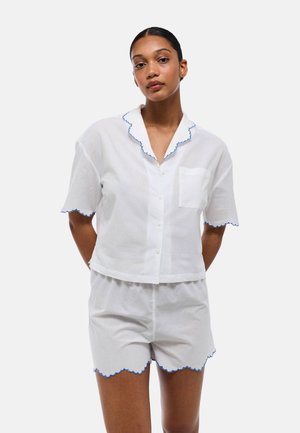 Ensemble en coton blanc comprenant une chemise col avec un bord festonné bleu et une poche, ainsi que des shorts assortis avec un ourlet festonné.