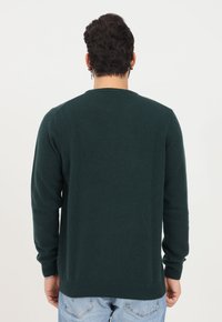 Maglione a maglia verde scuro con collo rotondo, maniche lunghe e polsini e bordo a costine. Texture liscia, design semplice e silhouette aderente.