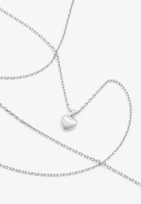 Silberne Halskette mit feiner Kette und kleinem, gebürstetem Herzanhänger. Die Kette besitzt ein klassisches Gliederdesign. Minimalistisch und elegant.