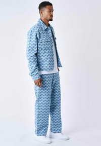 Giacca di jeans blu e pantaloni con un motivo geometrico in diverse tonalità di blu. Completati con sneakers bianche.