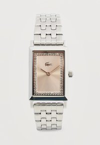 Montre-bracelet rectangulaire en argent avec bracelet métallique à maillons, cadran en or rose, bordure en cristal, deux aiguilles fines et un petit logo de crocodile à midi.
