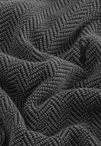 Tessuto a motivo houndstooth grigio con una consistenza morbida, caratterizzato da una leggera lucentezza e da un piccolo logo ricamato nell'angolo in basso a destra.