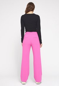 Zwarte langemouwen shirt gecombineerd met hoge taille, wijde broek in felroze, met een elastische tailleband en twee achterzakken.