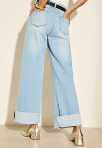 Jeans a gamba larga di colore blu chiaro con orlo risvoltato, dotati di due tasche posteriori e una cintura nera. Il tessuto ha una morbida trama in denim.