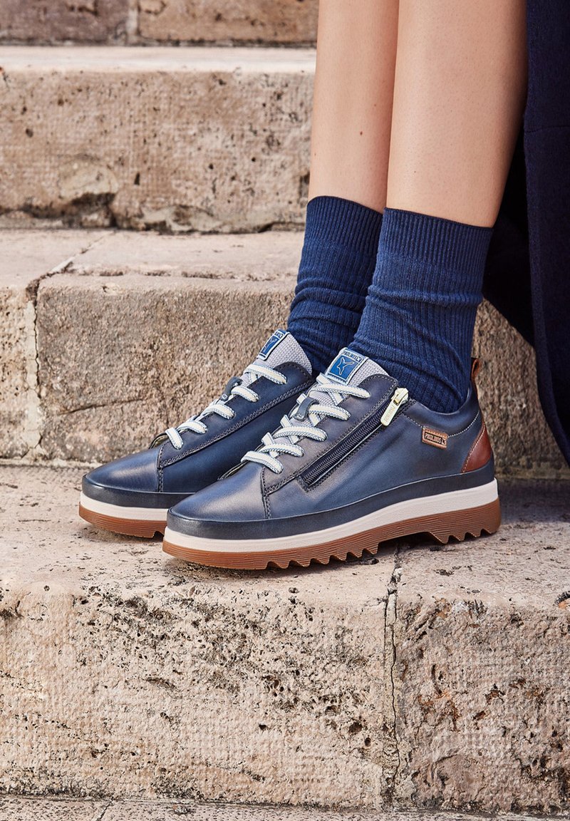 Navy leather sneakers featuring a textured surface, lace-up design, and side zipper. Details include light blue laces and brown accents.