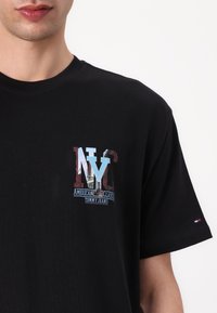 Zwart katoenen t-shirt met een kleurrafische "NYC" afbeelding van gebouwen, vergezeld van de teksten "American Classic" en "Tommy Jeans". Korte mouwen.