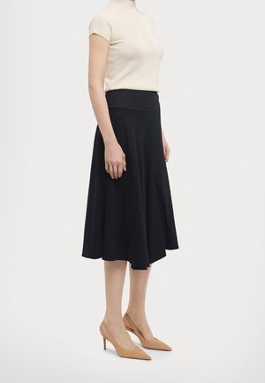 Czarna rozkloszowana spódnica z dopasowaną talią, wykonana z miękkiego materiału. Połączona z jasnobeżowym krótkim topem oraz cielistymi butami na wysokim obcasie.