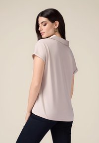 Lichtbeige polo shirt met korte mouwen, een kraag en opgerolde mouwen, gemaakt van zachte stof, gedragen met donkere, aansluitende broek.
