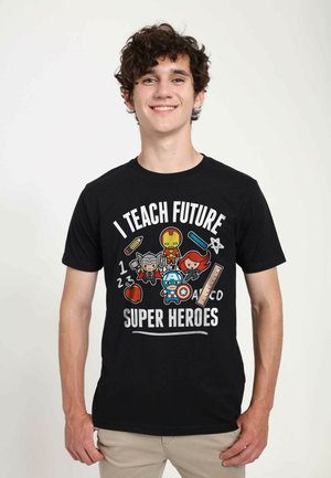 Schwarzes Baumwoll-T-Shirt mit Designs von Cartoon-Superhelden, dem Text "ICH UNTERRICHTE ZUKÜNFTIGE SUPERHELDEN" und bunten Akzenten von Schulmaterialien.