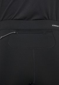 Leggings sportivi neri con una texture liscia, dotati di una tasca con zip sicura e una vita elastica con il marchio "AEROREADY".