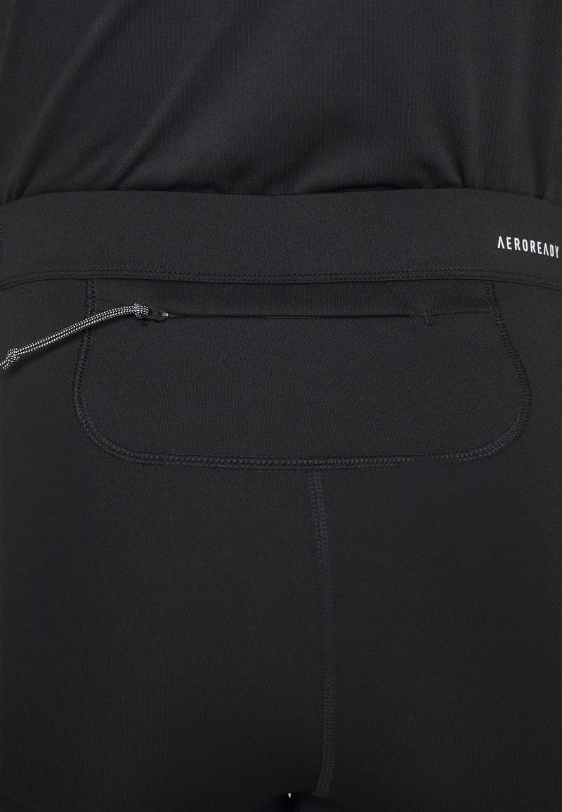Zwarte sportleggingen met een gladde textuur, voorzien van een veilige ritszak en een elastische tailleband met "AEROREADY" branding.