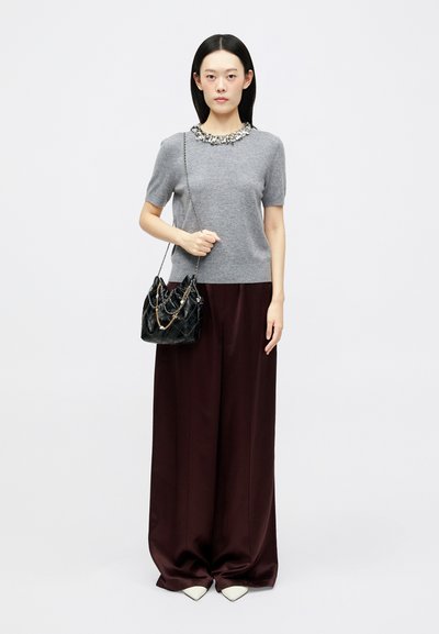 Harmaa lyhythihainen neule, jossa on koristeltu kaulus, yhdistettynä väljään tumman viininpunoiseen housupukuun ja pieneen mustaan, tikattuun käsilaukkuun, jossa on ketjuyksityiskohtia.