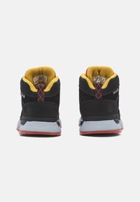 Czarne zamszowe trampki typu high-top z żółtym wykończeniem, czerwonymi akcentami i szarą podeszwą. Posiadają wyściełany kołnierz i teksturowany panel z tyłu.