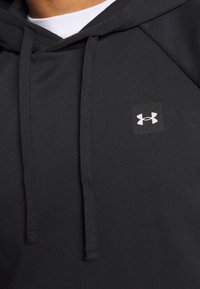 Sudadera con capucha en tejido negro con un parche de logo cuadrado, cordones y una textura suave. El diseño presenta mangas raglán.