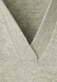 Gros plan sur un tissu de pull beige tricoté avec un col en V côtelé en laine douce.