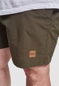 Khaki šortky vyrobené z ľahkého materiálu, s textúrovaným povrchom a obdĺžnikovou nálepkou Urban Classics na dolnej ľavej nohe.