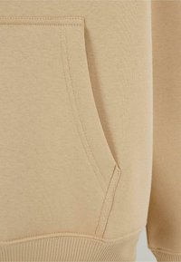 Beige sweatsweaterstof met een kangoeroezak, ribbelzoom en dubbel gestikte naden voor extra duurzaamheid. Zachte textuur.