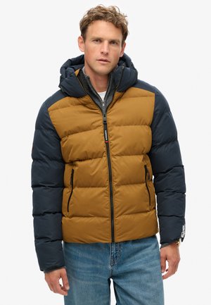Chaqueta tipo plumón con capucha en colores marrón y azul marino, con textura acolchada, cremallera frontal y dos bolsillos laterales.