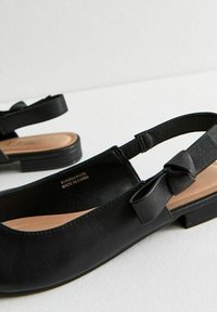 Svarta läderslingbacksandaler med en mjuk innerfoder, platt häl och en båge på sidan. Sulan är texturerad för bättre grepp.