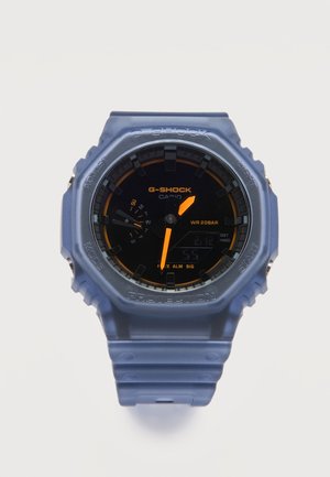 Blauwe Casio G-Shock polshorloge met zwarte wijzerplaat, oranje wijzers, dagindicator, digitaal display en robuust beschermend ontwerp.