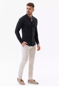 Navy-blue overhemd met lange mouwen en een mandarinnekraag, gecombineerd met crèmekleurige broek en beige bootschoenen, wat een casual uitstraling geeft.