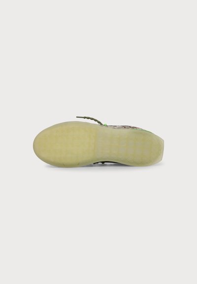 Semelle de chaussure avec une bande de roulement en caoutchouc jaune clair semi-transparente et un motif hexagonal visible, vue de dessous sur fond blanc.