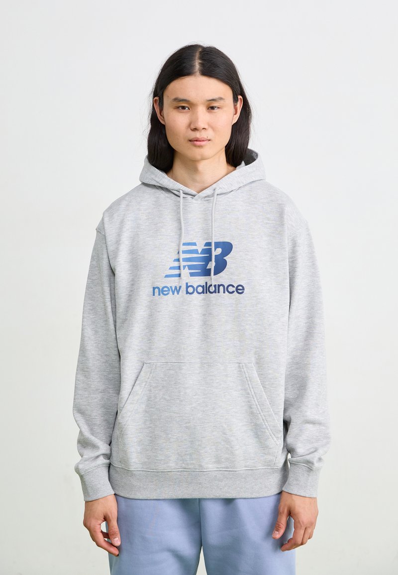 Siv hoodie z veliko sprednjo žepe, kapuco na vrvico in modrim logotipom 'New Balance'. Mehka tkanina s sproščenim krojem in rebrastimi manšetami.