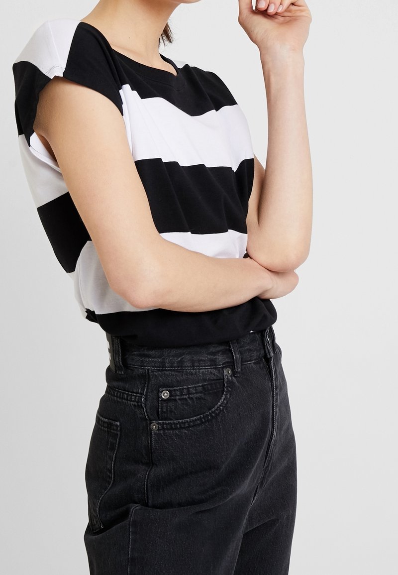 T-shirt à manches courtes noir et blanc rayé avec un col rond, associé à un jean noir taille haute. En matière coton doux, coupe décontractée.