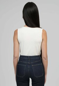 Débardeur blanc côtelé sans manches avec un col rond, associé à un jean bleu foncé taille haute avec des poches arrière et des coutures visibles.