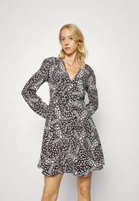 Vestido estampado em preto e branco com mangas longas, decote em V e cintura ajustada, apresentando uma saia rodante e tecido texturizado.