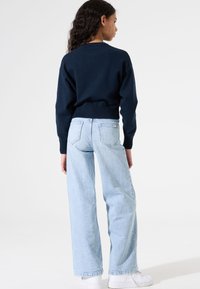 Sweatshirt cropped bleu marine avec ourlet côtelé, associé à un jean bleu clair à jambes larges. Le modèle porte des baskets blanches, vu de dos.