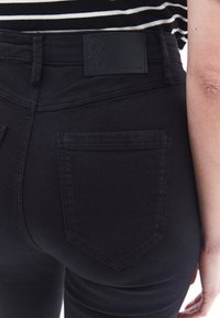 Jeans de mezclilla negra de cintura alta, con una textura suave, bolsillos traseros y una etiqueta de cuero con la marca en la cintura.