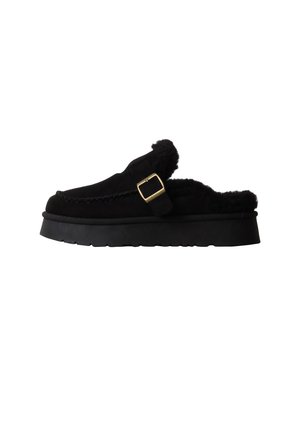 Mocassin noir à enfiler avec semelle épaisse, bride avec boucle dorée et doublure en fourrure douce visible autour de l'ouverture.
