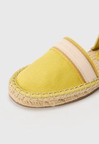 Espadrille gialla in canvas con suola in juta intrecciata, dotata di una banda a strisce beige e rosa nella parte anteriore. I dettagli cuciti aggiungono texture.