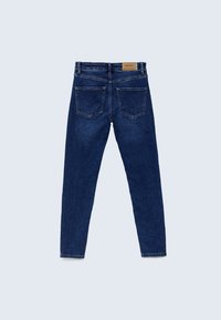 Jean en denim bleu foncé vu de dos avec deux poches arrière et une petite étiquette de marque beige sur la ceinture.