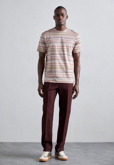 T-shirt a righe, maniche corte, di colore beige con linee multicolori; abbinato a pantaloni bordeaux scuro e sneaker basse con un motivo testurizzato.