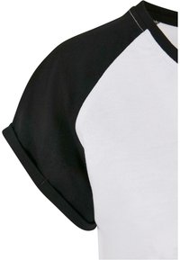 Gros plan d'un T-shirt blanc avec manches raglan noires et col rond noir.
